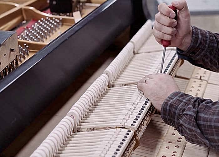A close-up of a technician using a screwdriver to adjust the internal mechanisms of a piano, highlighting professional maintenance and care.